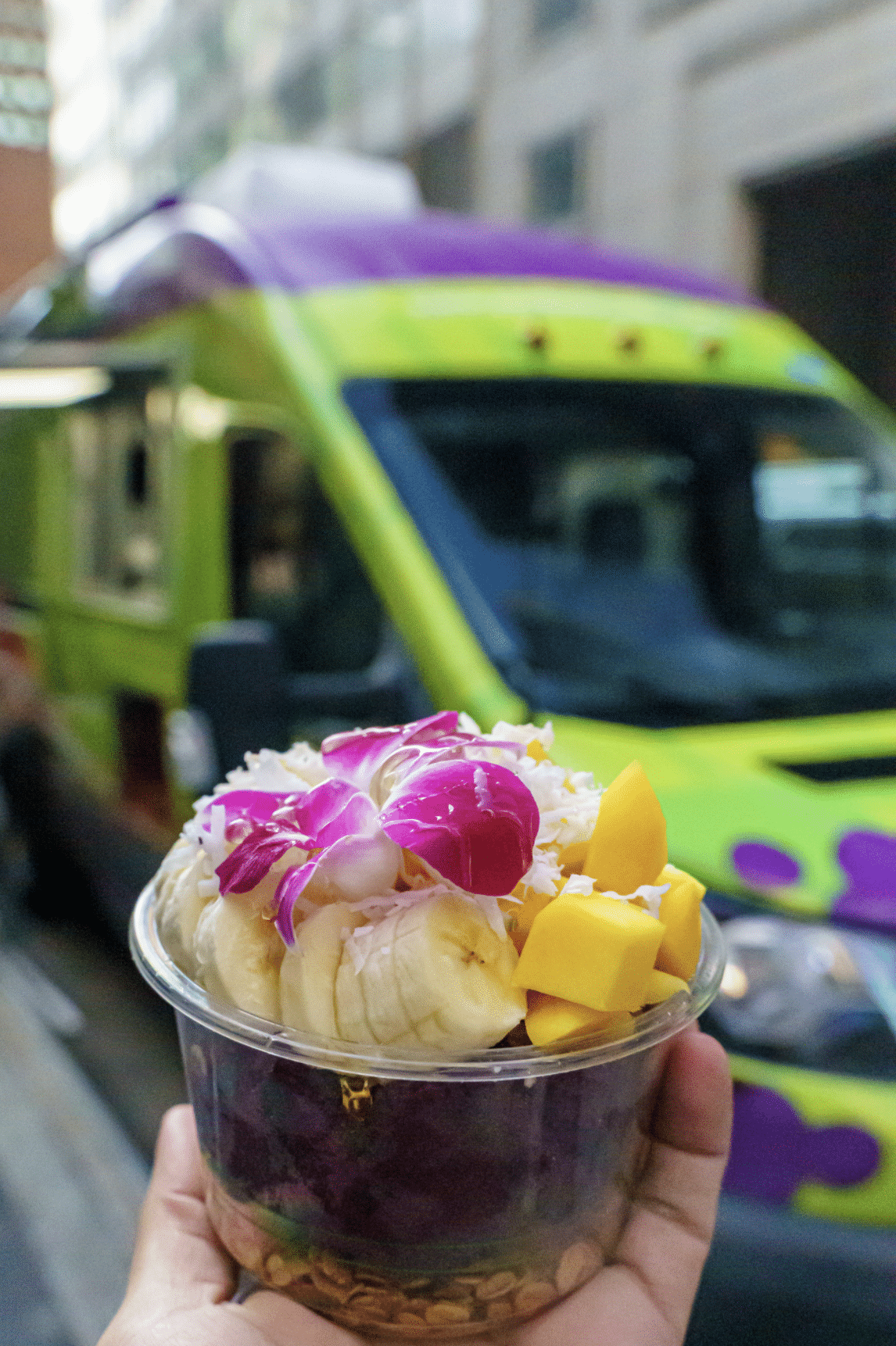 Acai Bowl topped with mango, banana, and coconut flakes, in front of food truck
