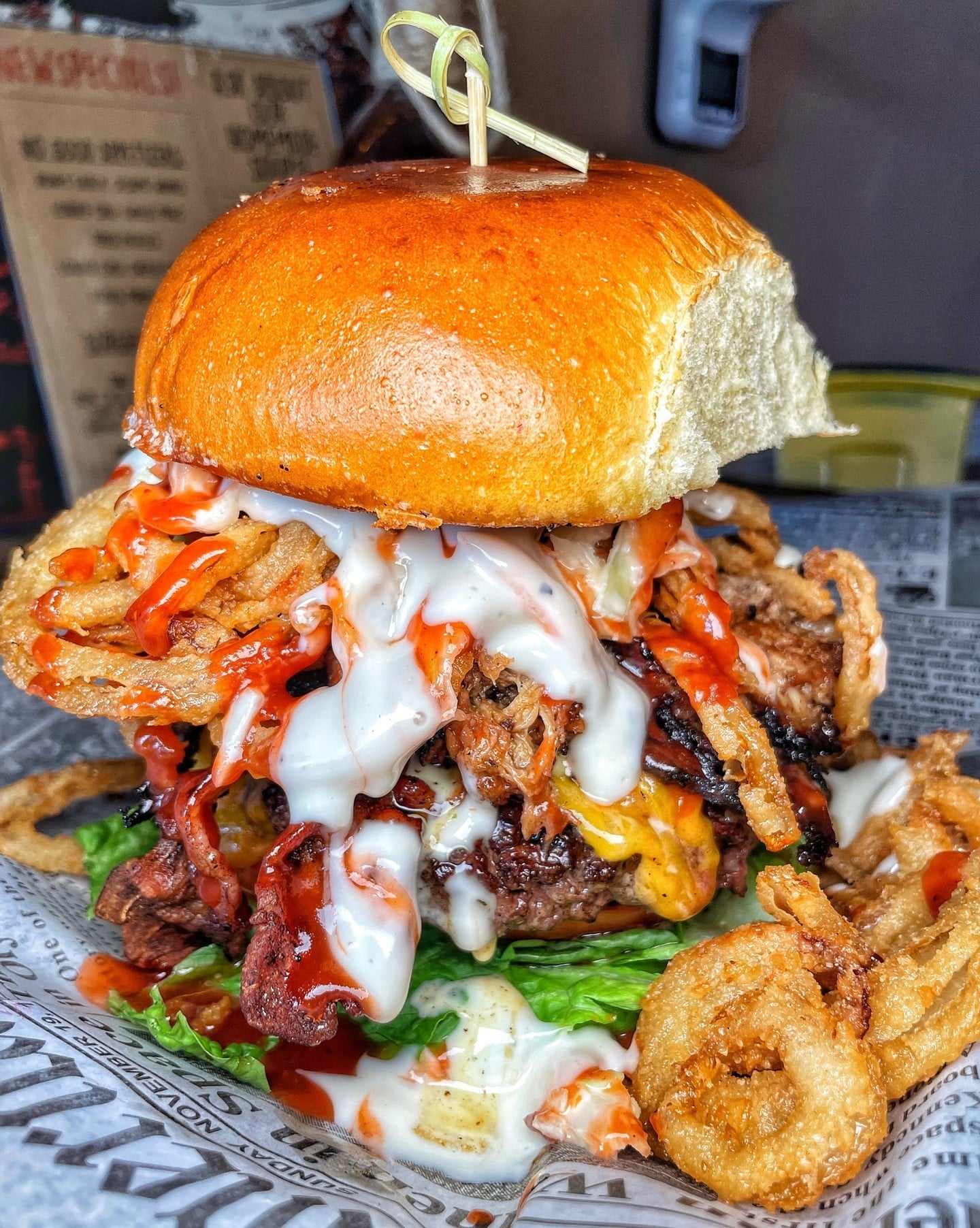 Burger topped with barbecue pulled pork, crispy bacon, cheddar, lettuce, tomato, cripsy onion straws, and cole slaw smothered with a barbecue and ranch combo served on a brioche bun.