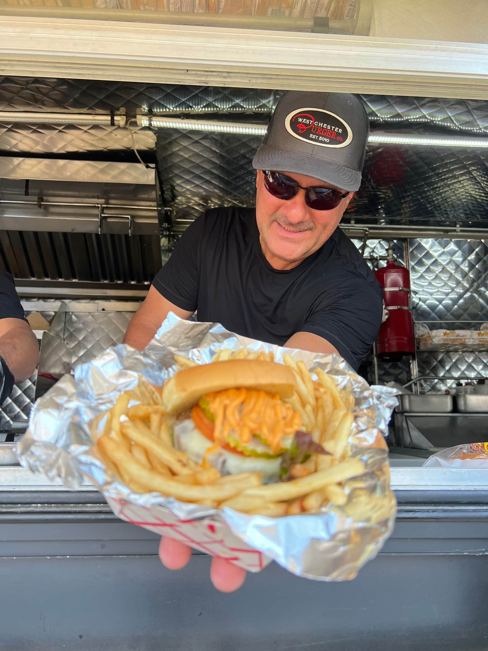 Westchester burger food truck owner holding burger from his food truck window
