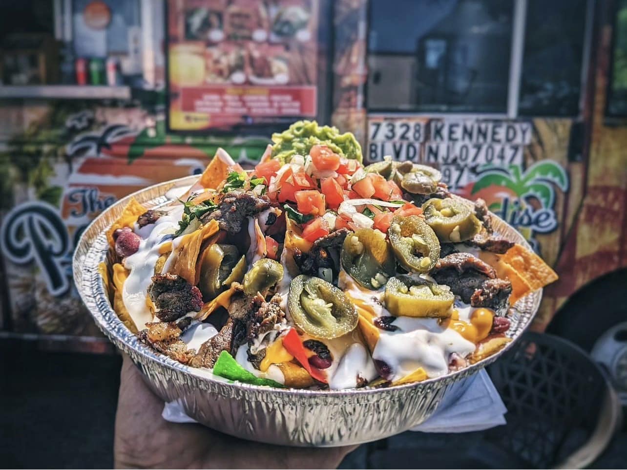 a takeout container of loaded nachos with meat