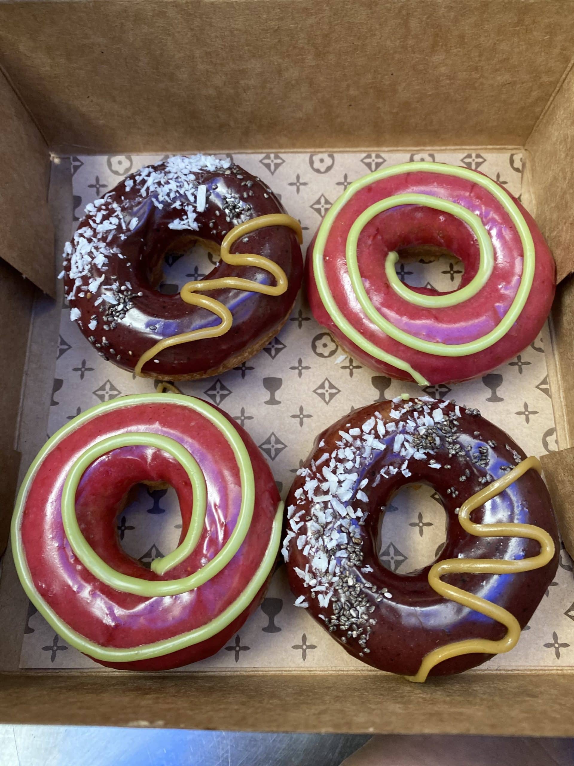 Box of four donuts with two different flavors including chocolate coconut and strawberry