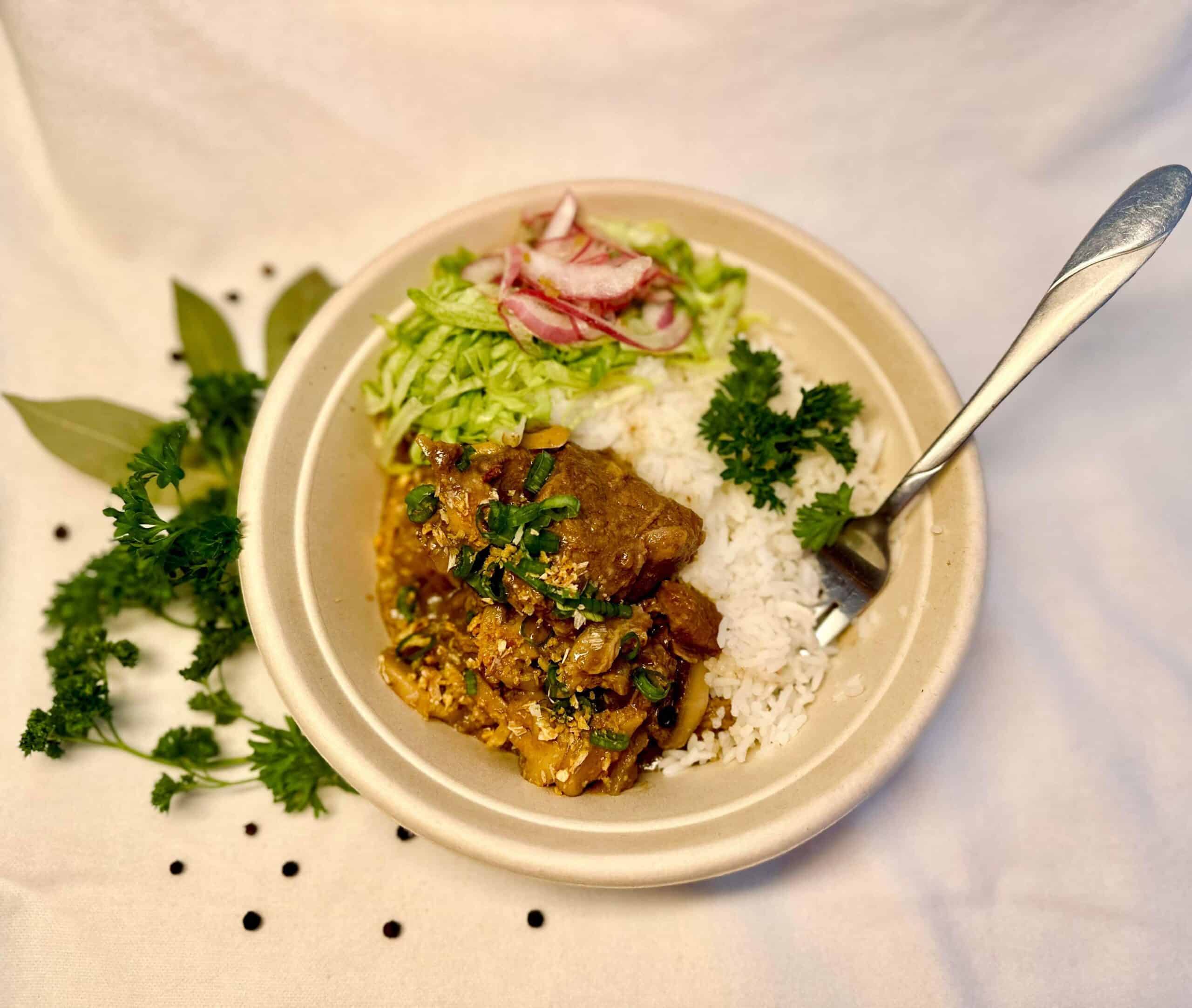 bowl of braised beef over rice with a side of greens and radishes