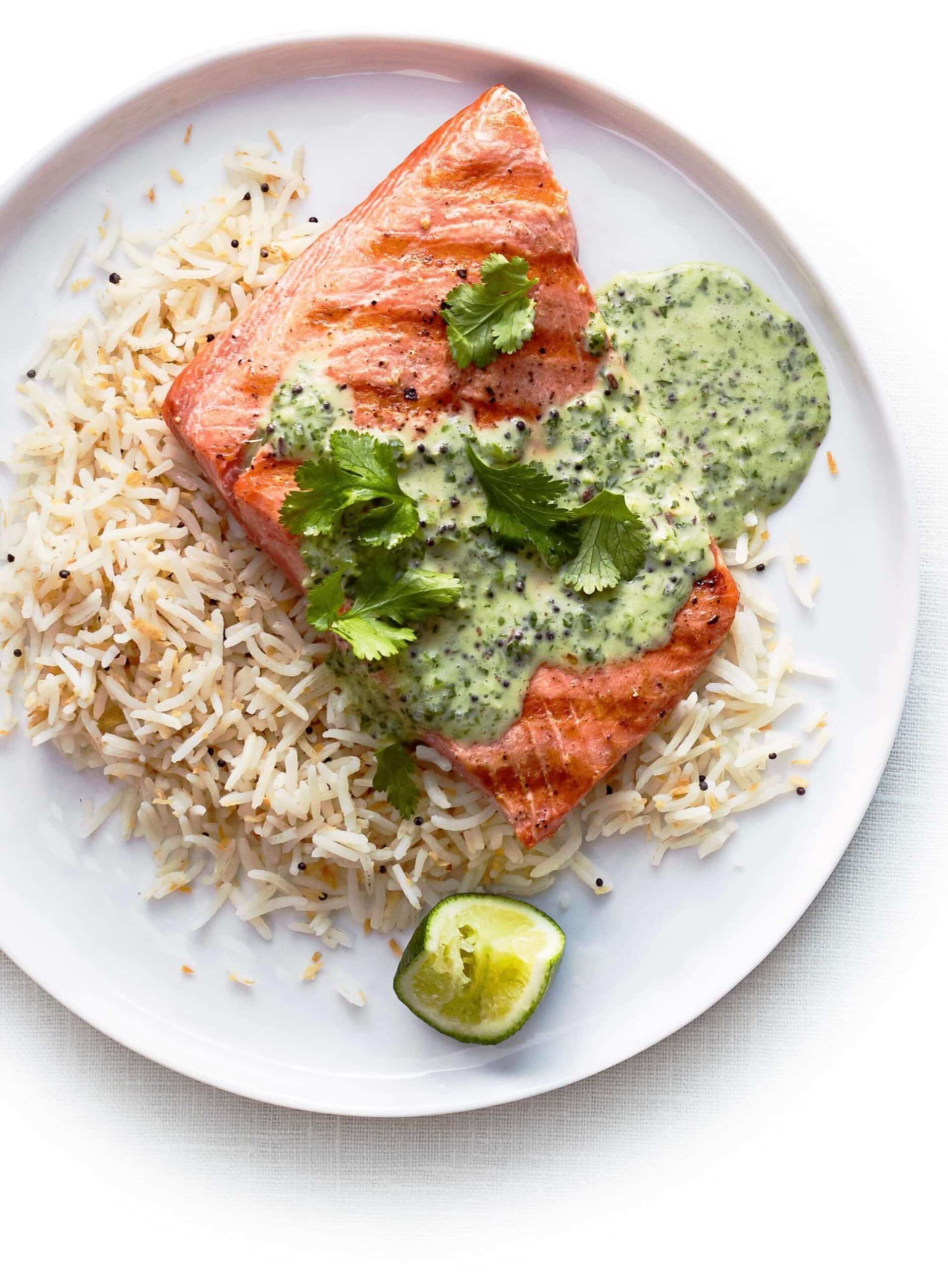 plate of grilled salmon over rice with a green sauce and herb topping