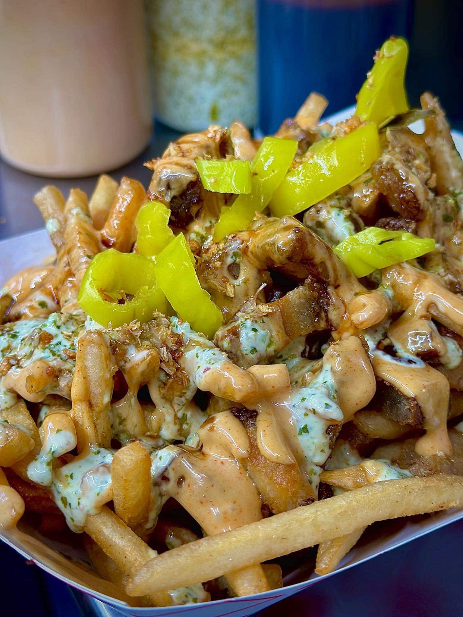 close-up view of loaded fries with sauces drizzled over it topped with sliced banana peppers